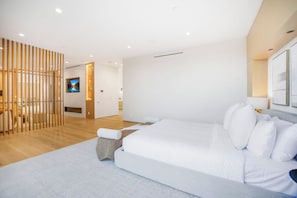 A modern bedroom with a large bed, a wooden partition, and a TV in the background. - Oak Pass Manor (Beverly Hills)