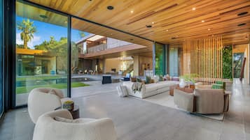 Um interior moderno com uma grande parede de vidro, teto de madeira e área de estar com sofás e mesa de centro.