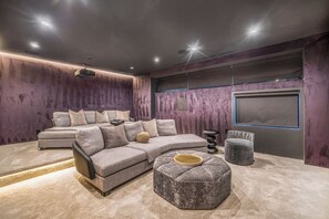 A modern living room with a sectional sofa, ottoman, and a flat-screen TV mounted on the wall. - Oak Pass Manor (Beverly Hills)