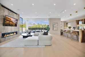 A modern living room with a fireplace, a dining area, and a kitchen with bar stools. - Amestoy Modern (Encino)