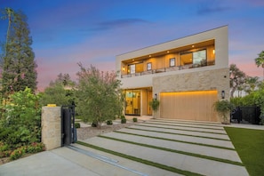 A modern two-story house with a stone facade, a large garage, and a well-maintained lawn. - Amestoy Modern (Encino)