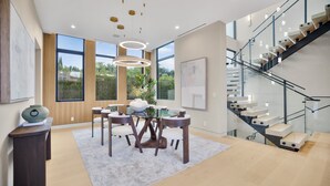 Un interior moderno con zona de comedor, escalera y ventanas amplias.