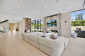 A spacious living room with a large sectional sofa, a flat-screen TV mounted on the wall, and a fireplace. - Amestoy Modern (Encino)