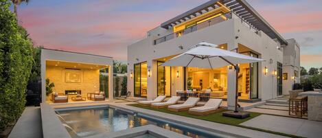 Una casa moderna de dos pisos con piscina, mobiliario exterior y un interior bien iluminado.