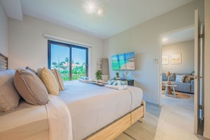 Ein Schlafzimmer mit einem großen Bett, einem Fernseher und Blick auf Grünflächen.