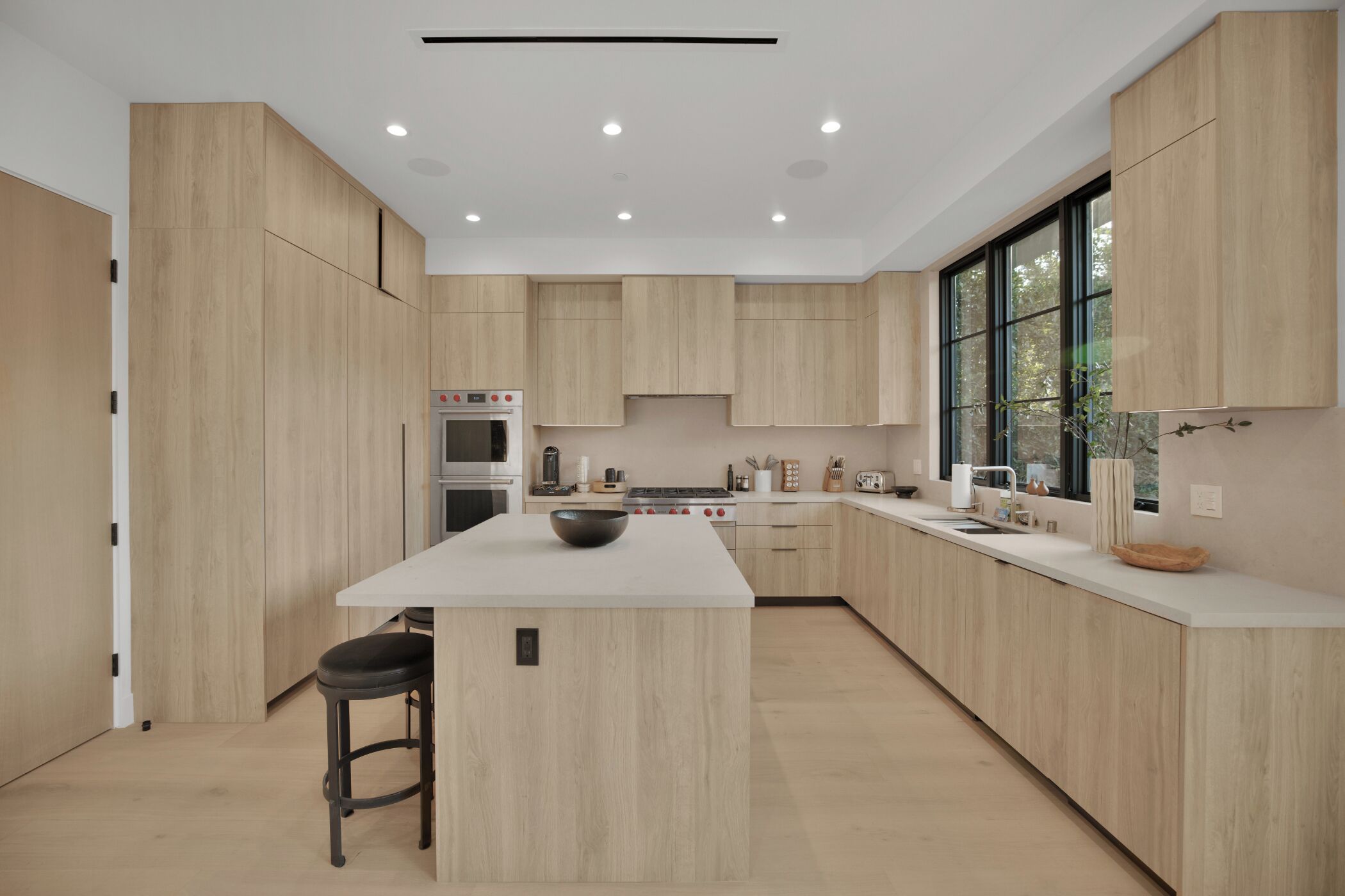 A modern kitchen with wooden cabinets, a central island, and a large window.