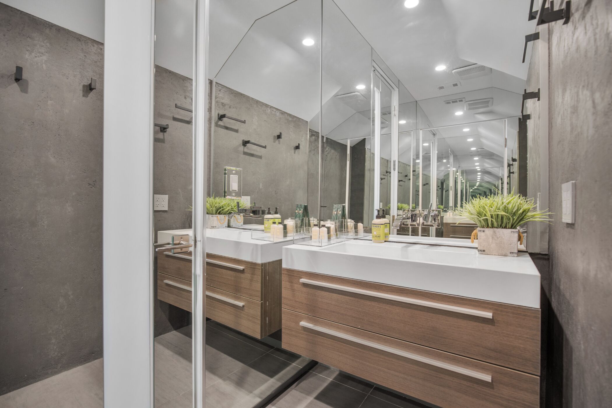 Une salle de bain moderne avec un grand miroir, des meubles en bois et une plante en pot.