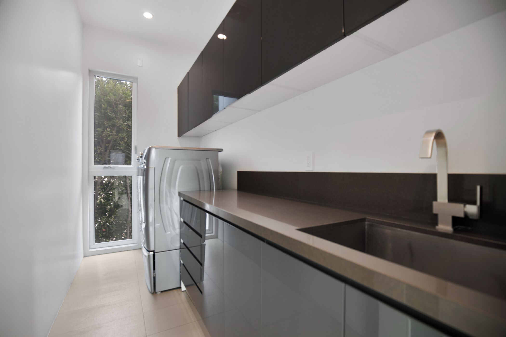 A modern kitchen with a built-in refrigerator, a stainless steel sink, and a window providing a view of trees.