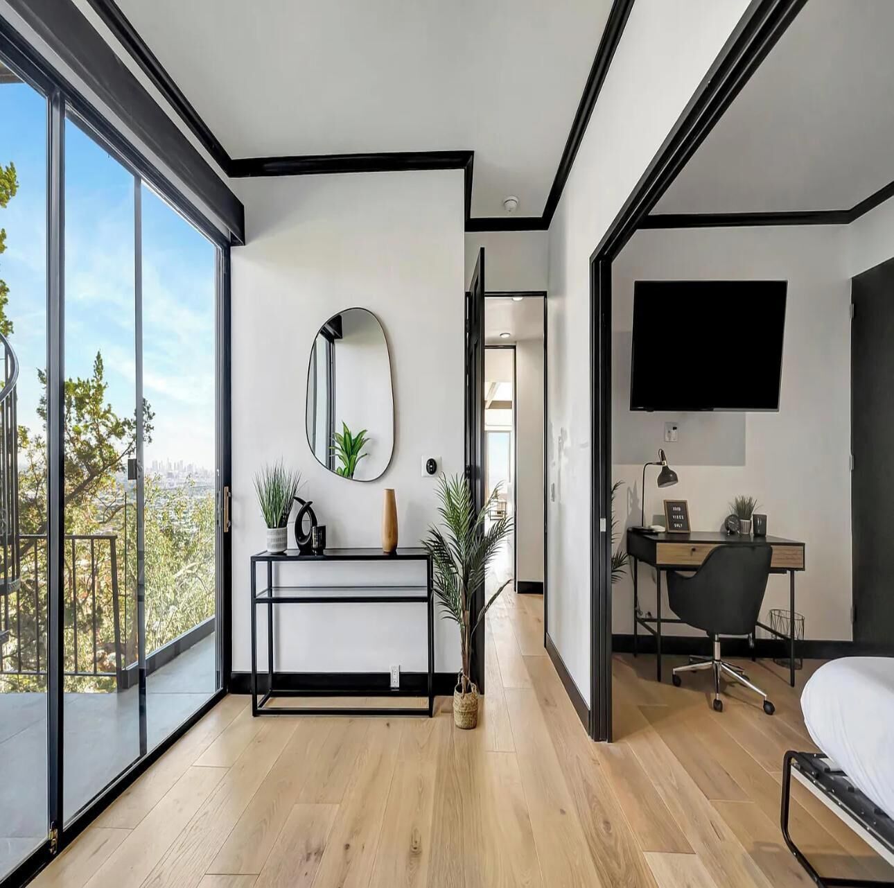A modern bedroom with a large window, a desk, a chair, and a bed.