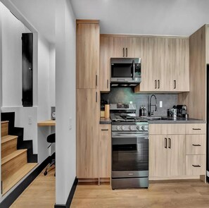 A modern kitchen with wooden cabinets, a stainless steel stove, and a microwave. - Skyview Estate (West Hollywood)