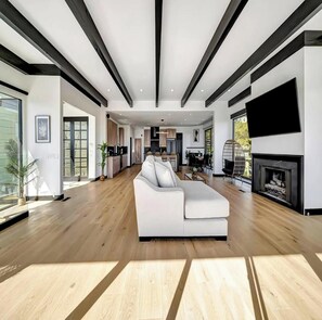 A spacious living area with a white sofa, wooden flooring, and a fireplace. - Skyview Estate (West Hollywood)