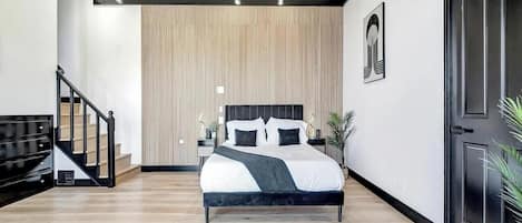 A modern bedroom with a large bed, a wooden slatted wall, a staircase, and a black door.