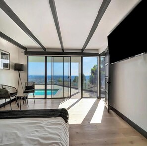 Un dormitorio con una cama grande, un escritorio, una silla y vistas a una piscina y al océano.