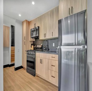 Una cocina moderna con armarios de madera, un refrigerador de acero inoxidable, un microondas, una estufa y un fregadero.