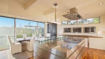 A modern kitchen with a glass island, stainless steel appliances, and a large window overlooking a scenic view.