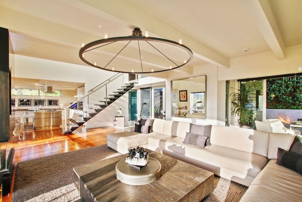 A spacious living area with a modern staircase, a large sofa set, and a unique circular ceiling light fixture. - Beverly Horizon (Beverly Hills)