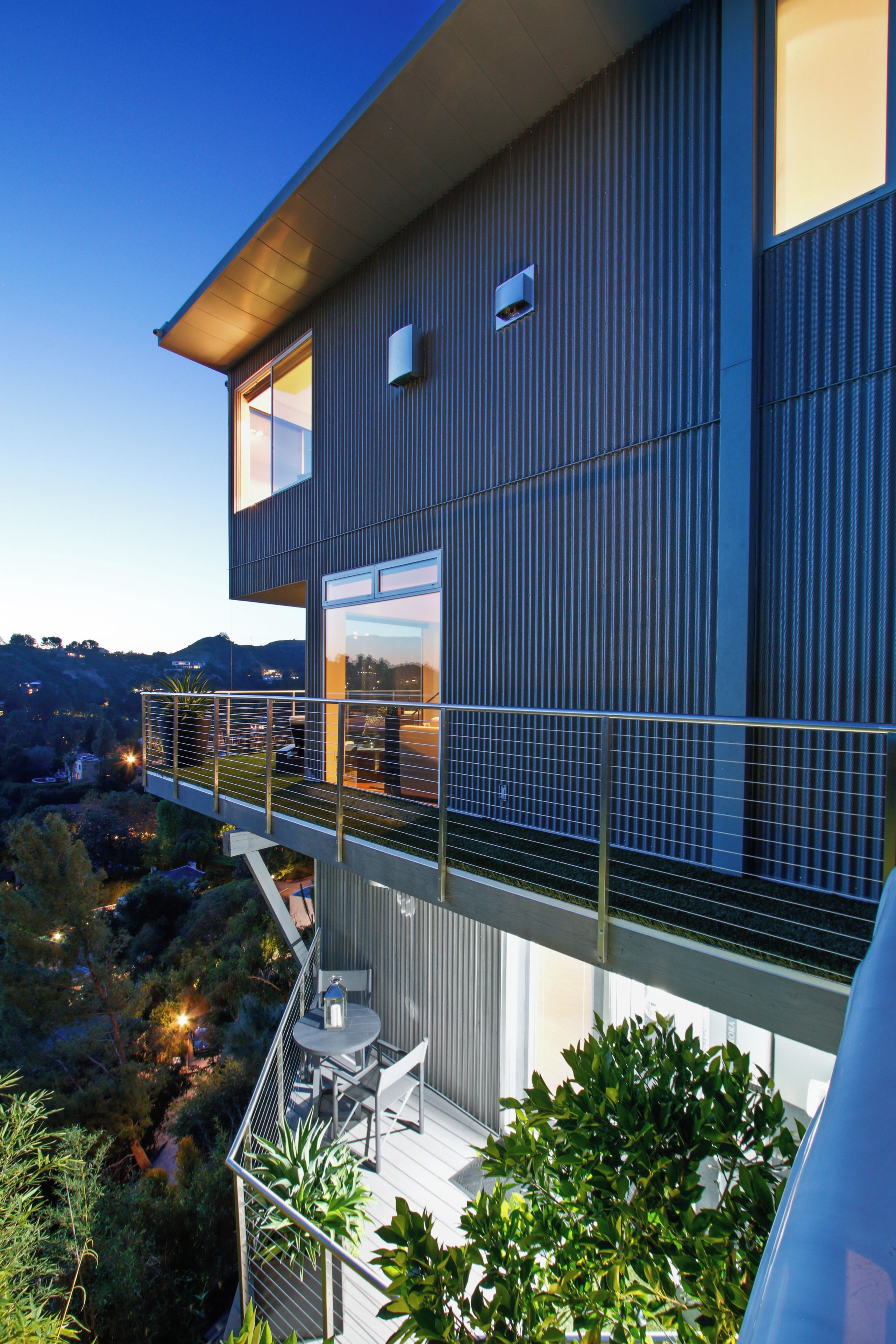 Une maison moderne à deux étages, dotée d’un balcon, d’un espace salon extérieur et offrant une vue sur le paysage environnant.