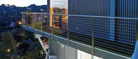 Une maison moderne à deux étages, dotée d’un balcon, d’un espace salon extérieur et offrant une vue sur le paysage environnant.