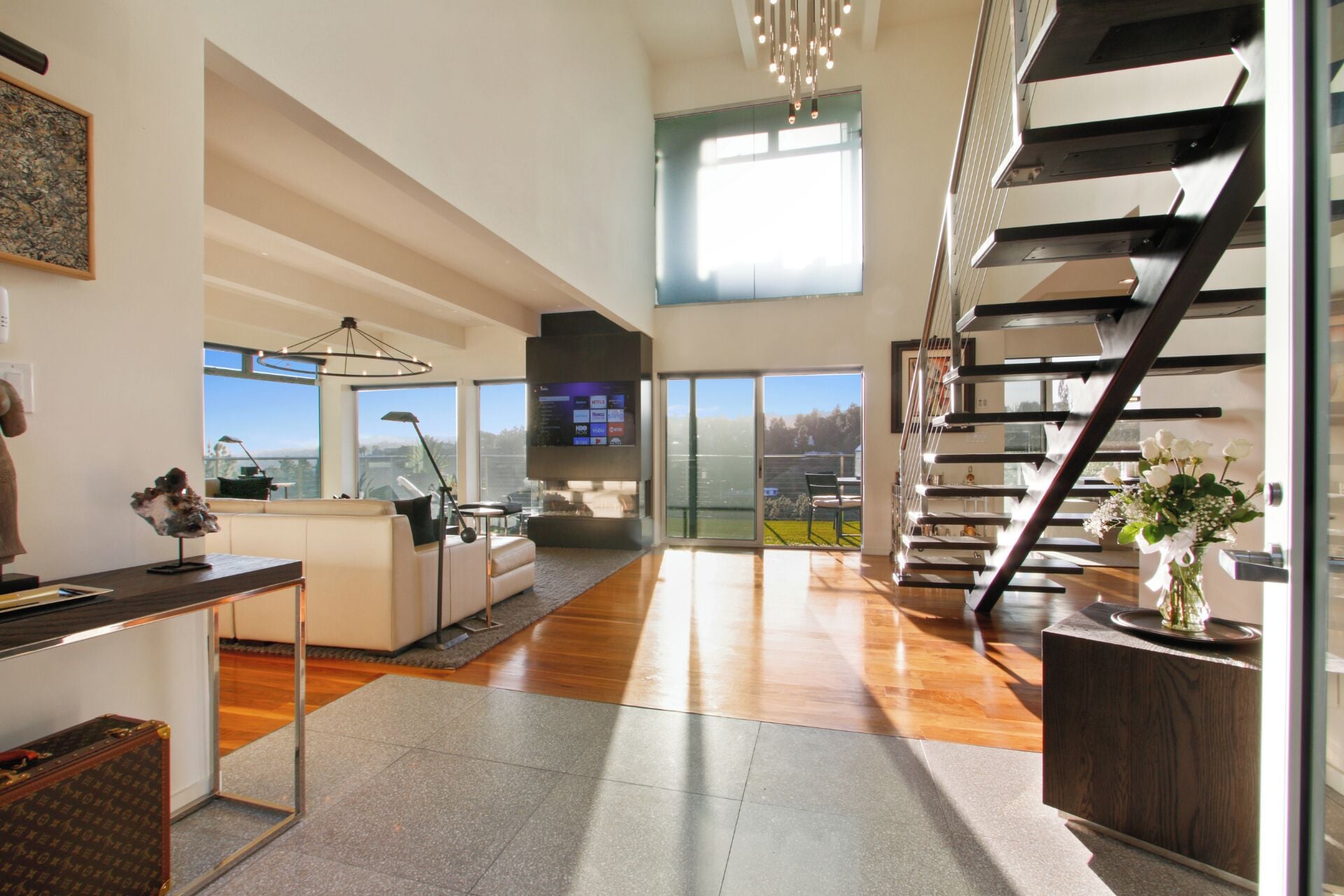 Uma sala de estar espaçosa com escada moderna, TV de tela plana e uma grande janela com vista para o exterior.