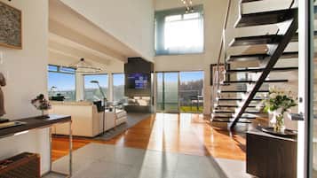 Uma sala de estar espaçosa com escada moderna, TV de tela plana e uma grande janela com vista para o exterior.
