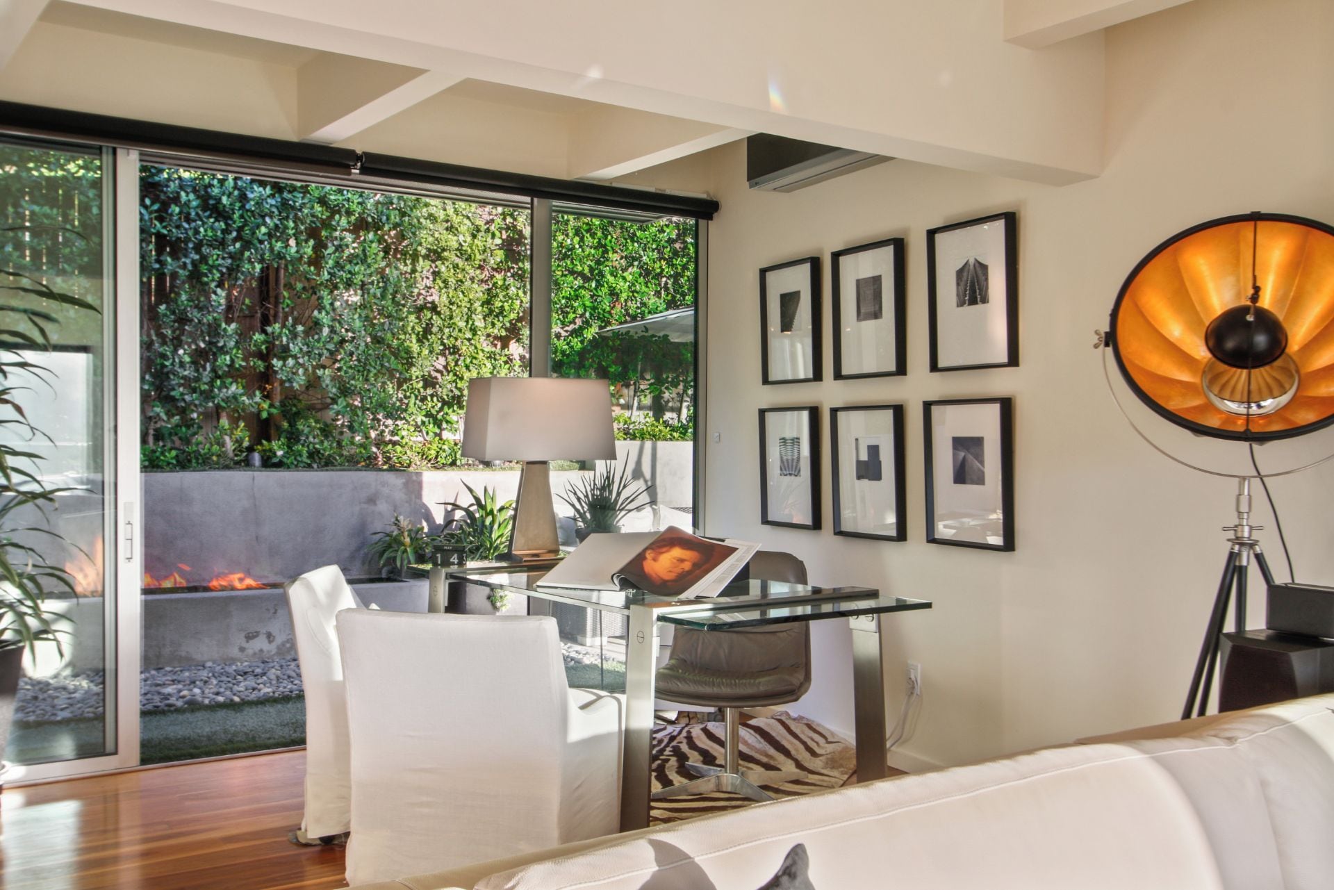 Un salon moderne avec une table en verre, des meubles blancs et une grande fenêtre donnant sur un espace verdoyant.