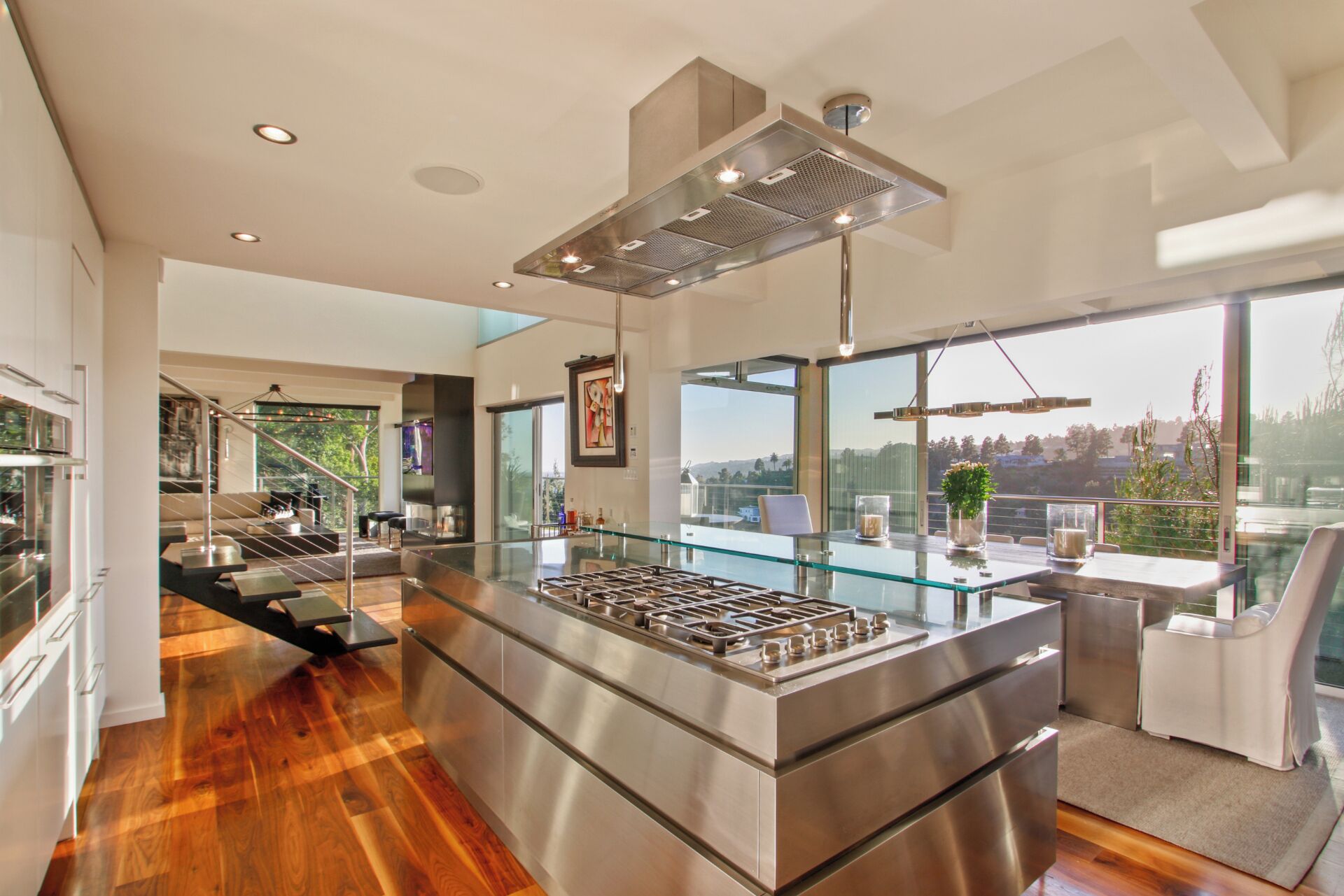 Uma cozinha moderna com uma ilha central, eletrodomésticos de aço inoxidável e grandes janelas com vista para o exterior.
