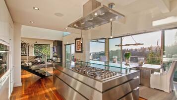 Uma cozinha moderna com uma ilha central, eletrodomésticos de aço inoxidável e grandes janelas com vista para o exterior.