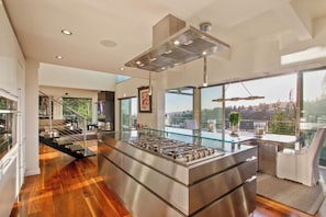 A modern kitchen with a central island, stainless steel appliances, and large windows offering a view of the outdoors. - Beverly Horizon (Beverly Hills)