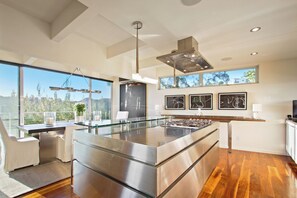 Cozinha moderna com ilha central, eletrodomésticos de aço inoxidável e amplas janelas com vista para o exterior.