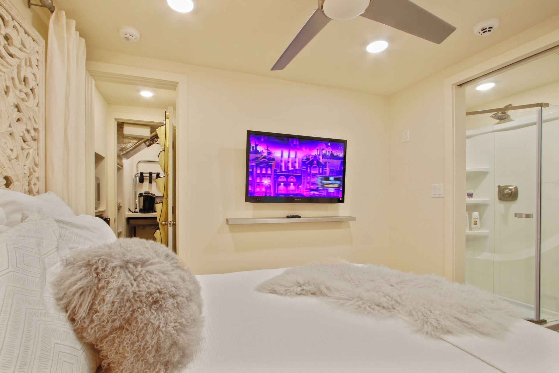 A hotel room with a bed, a TV mounted on the wall, a ceiling fan, and a shower area.