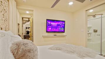 A hotel room with a bed, a TV mounted on the wall, a ceiling fan, and a shower area.