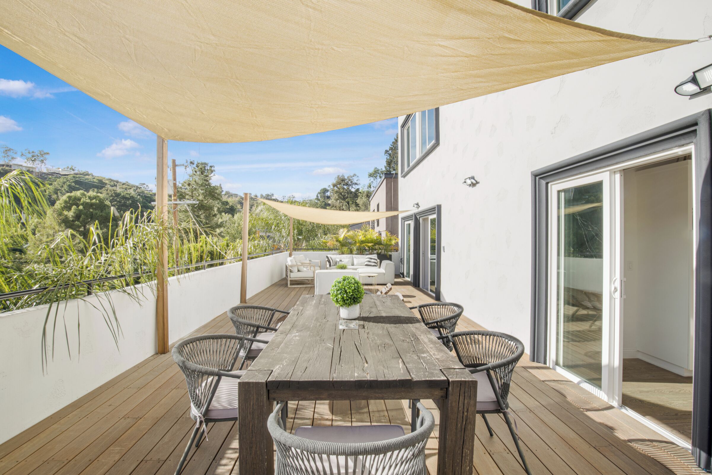 Une terrasse en bois avec une table et des chaises, un canapé et une grande fenêtre.