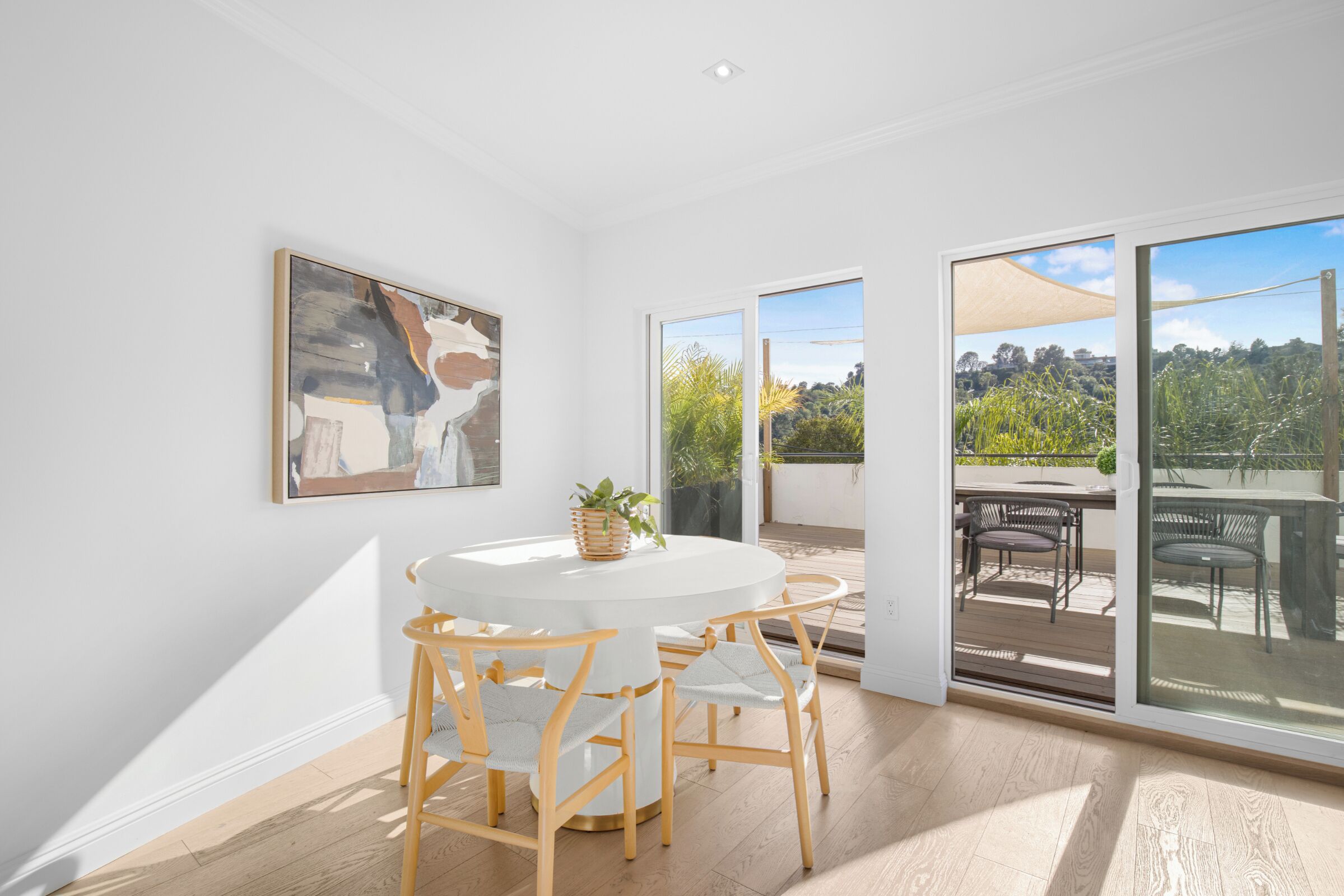 A room with a round table and chairs, a painting on the wall, and a view of an outdoor patio with furniture.