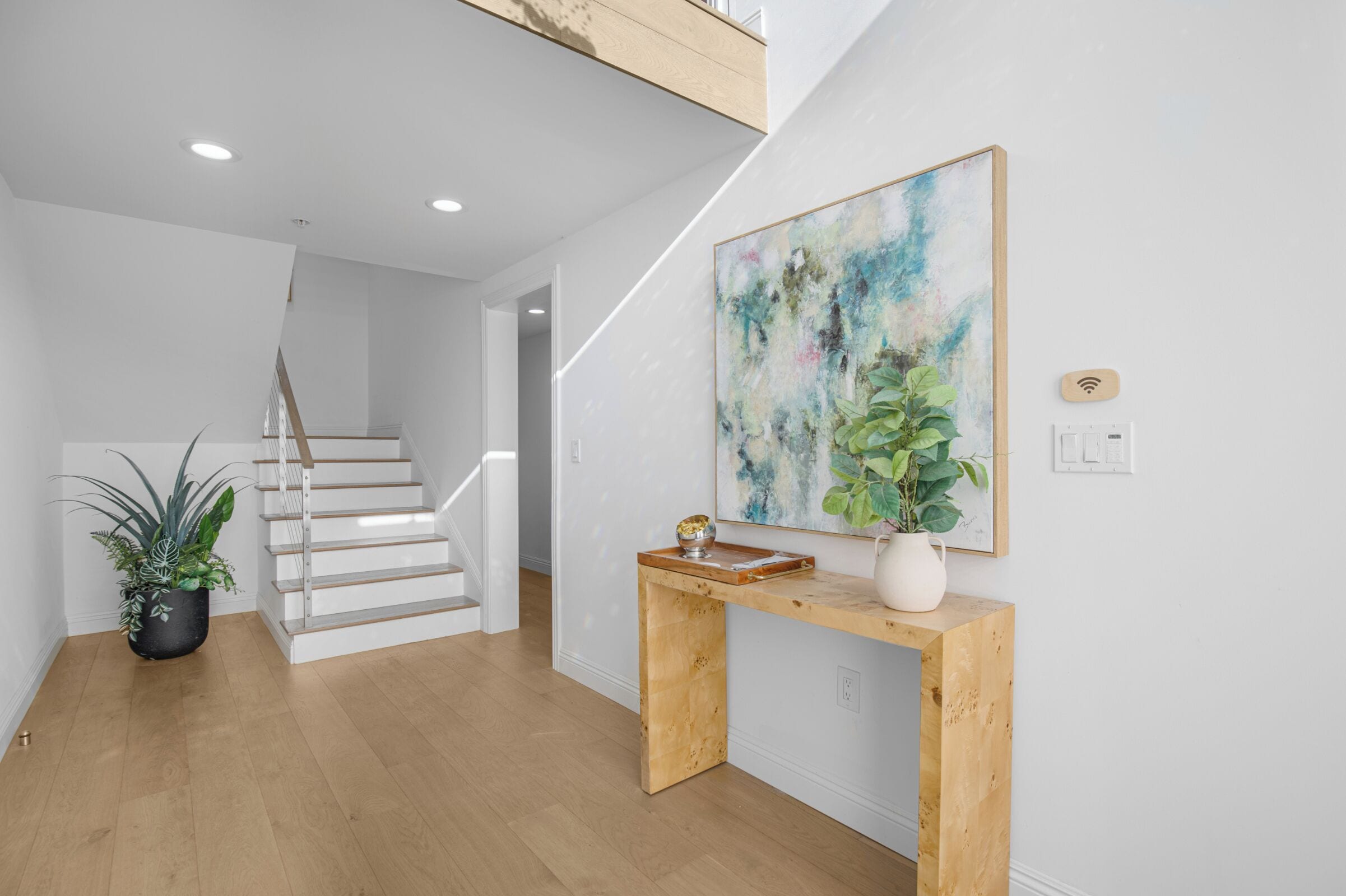 A modern interior with a staircase, a console table with a plant, and a large abstract painting.