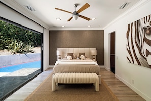 A modern bedroom with a large bed, a ceiling fan, and a view of a swimming pool. - Valea Estate (Beverly Hills)