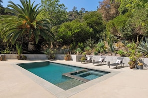Ein rechteckiger Pool mit klarem, blauem Wasser, umgeben von einer Betonplattform. Entlang des Poolrandes befinden sich Liegestühle mit Kissen.