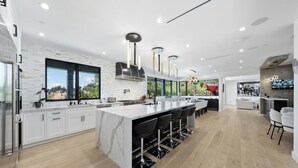 A modern kitchen with a large island, white cabinetry, and a view of the outdoors. - Oak Haven Sanctuary (Studio City)