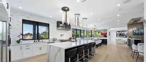 A modern kitchen with a large island, white cabinetry, and a view of the outdoors.
