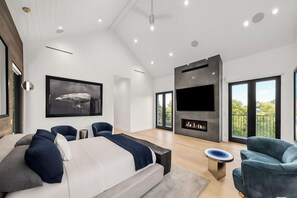 Quarto moderno com cama grande, lareira e TV na parede.