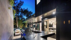 A modern kitchen with a marble countertop, a built-in oven, and a dining area with white chairs. - Oak Haven Sanctuary (Studio City)