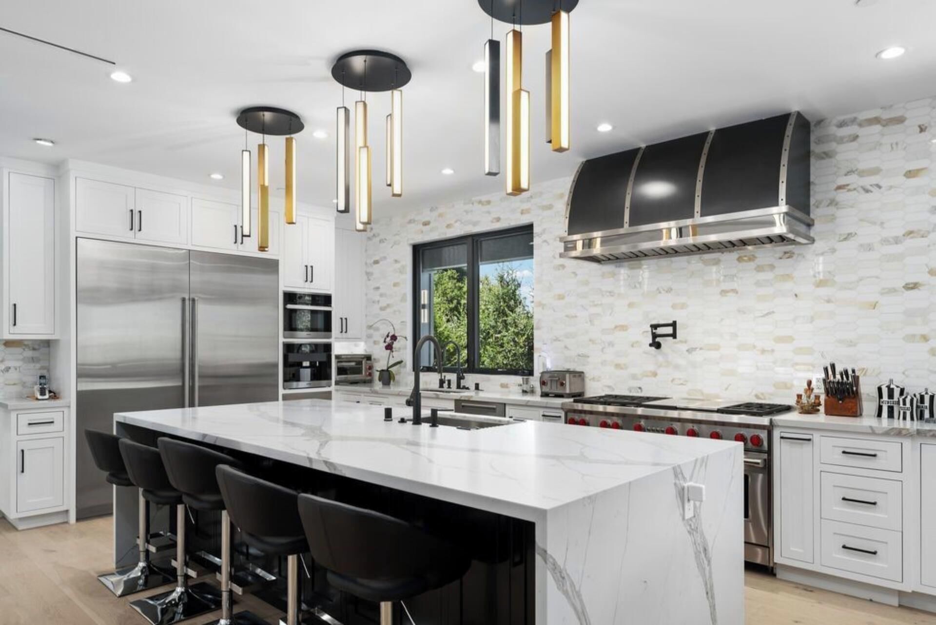 Cozinha moderna com uma ilha grande, eletrodomésticos de aço inoxidável e iluminação pendente.