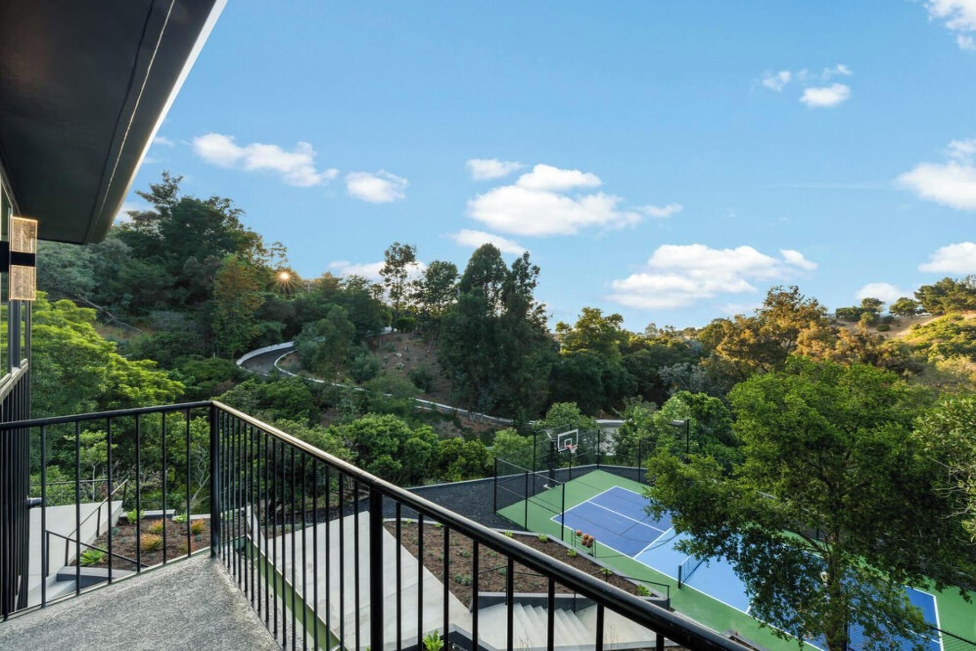 A tennis court surrounded by lush greenery and a winding road.
