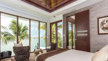 Quarto com uma cama grande, vista para o mar e varanda com uma cadeira.