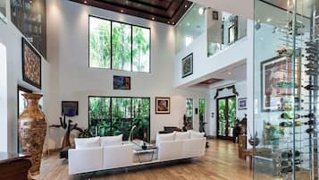 Uma sala de estar ampla, com um sofá branco, janelas grandes e uma vitrine de vidro.