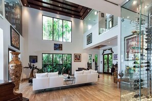 A spacious living area with a white sofa, large windows, and a glass display case. - Villa Teaka (Miami Beach)