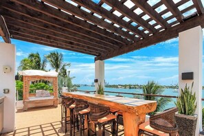 An outdoor patio with a wooden table and chairs, a pergola, and a view of the sea. - Villa Teaka (Miami Beach)