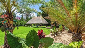 A tropical garden with a thatched-roof hut, lush greenery, and a well-maintained lawn. - Blockchain Manor (North Miami Beach)