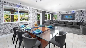 A modern kitchen with a glass dining table, grey chairs, and a grey sofa in the living area. - Blockchain Manor (North Miami Beach)