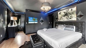 A modern bedroom with a large bed, a chandelier, a painting, and LED lighting. - Blockchain Manor (North Miami Beach)