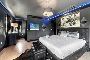 A modern bedroom with a large bed, a chandelier, a painting, and LED lighting. - Blockchain Manor (North Miami Beach)